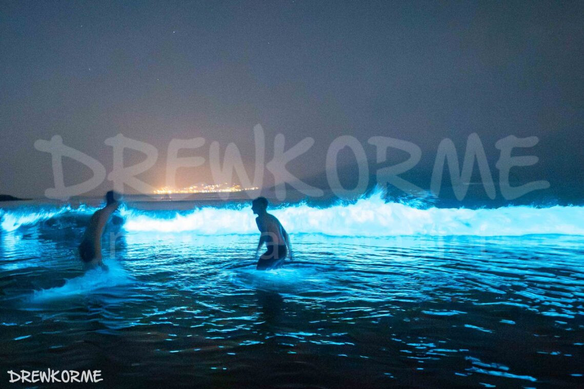 mar-de-ardora-area-das-vacas-cabana-de-bergantiños-costa-da-morte-galicia-drewkorme Dos personas bañándose en el mar de ardora en Area das Vacas, Cabana de Bergantiños, con olas bioluminiscentes iluminando el agua en la Costa da Morte, Galicia