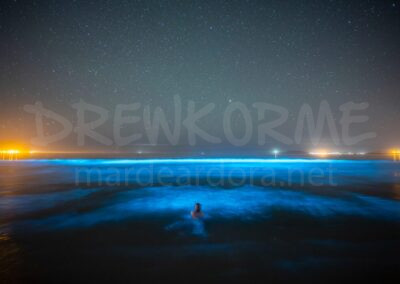 Mar de ardora en la Costa da Morte Galicia con bioluminiscencia azul en el mar y una persona en el agua bajo un cielo estrellado