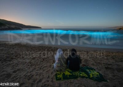 Mar de ardora en Rebordelo Cabana de Bergantiños Galicia con bioluminiscencia azul en la orilla y dos personas observando el fenómeno